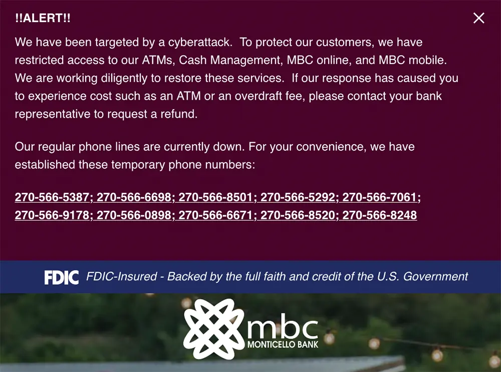 Screenshot from Monticello Banking Company's website displaying a cyberattack alert, with service restrictions on ATMs and online banking, and a list of temporary phone numbers due to downed regular lines.