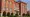 Red-brick Center Street School building with arched windows, shrubs and benches along its lawn.