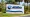 White roadside sign with blue “City of Columbia” lettering and a wave logo, surrounded by grass, shrubs and palm trees.
