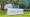 A sign reading “Ralph D. Turlington Florida Education Center” stands on a lawn beneath oak trees outside a glass-fronted building.